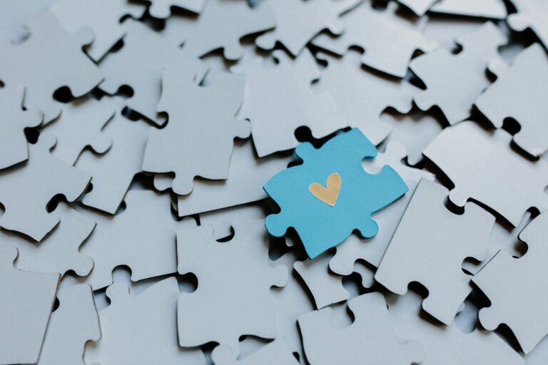 A blue puzzle piece with a yellow heart in the middle laying on top of gray puzzle pieces - YOU Psychiatry Clinic