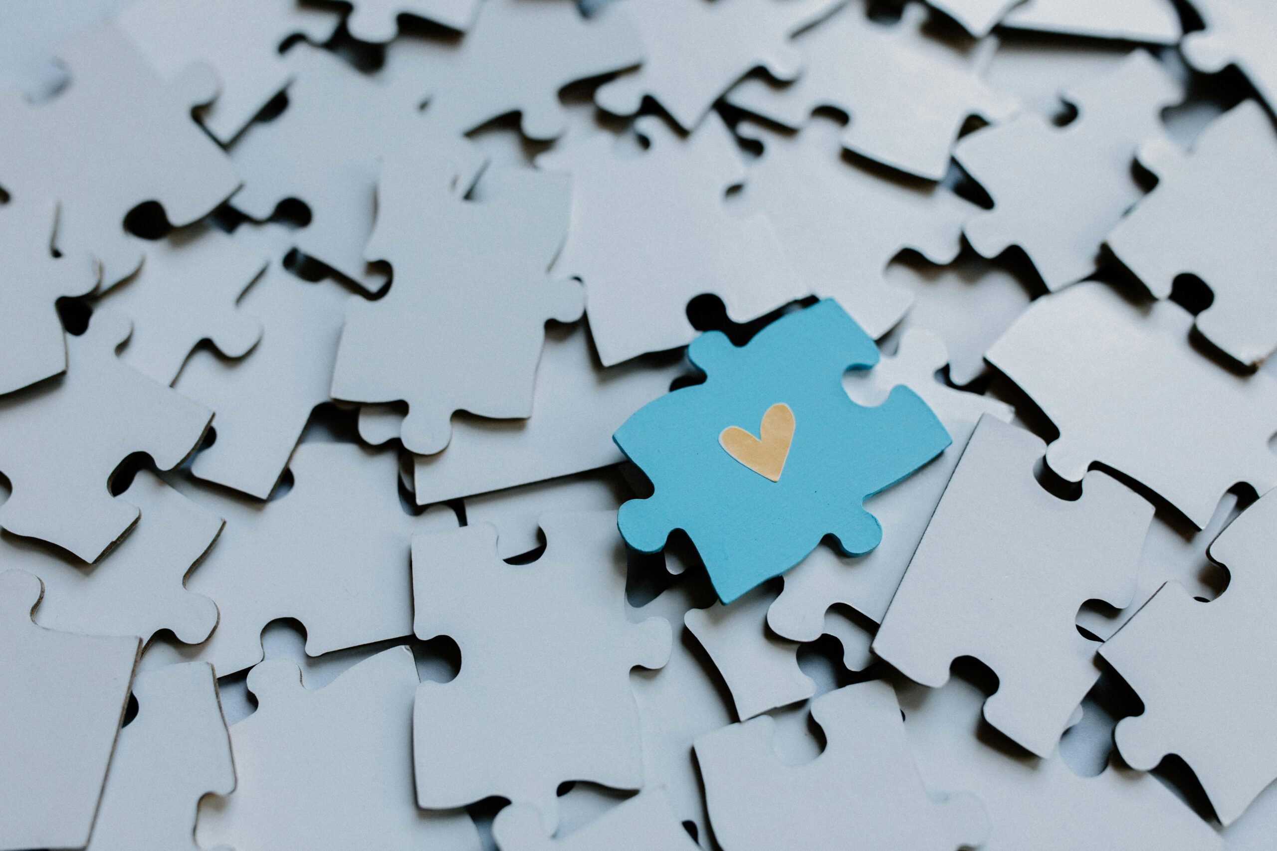 A blue puzzle piece with a yellow heart in the middle laying on top of gray puzzle pieces - YOU Psychiatry Clinic